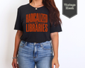 A woman wearing a vintage black graphic t-shirt with orange text that reads 'RADICALIZED BY LIBRARIES', paired with blue jeans. A badge in the top right corner reads 'Vintage Black'.