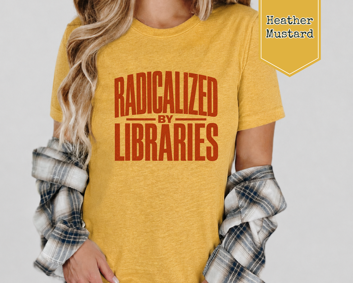 A woman wearing a heather mustard yellow graphic t-shirt with the text 'RADICALIZED BY LIBRARIES' in a distressed reddish-brown font. She has a plaid flannel shirt draped off her shoulders, and a yellow badge in the top right corner reads 'Heather Mustard'.
