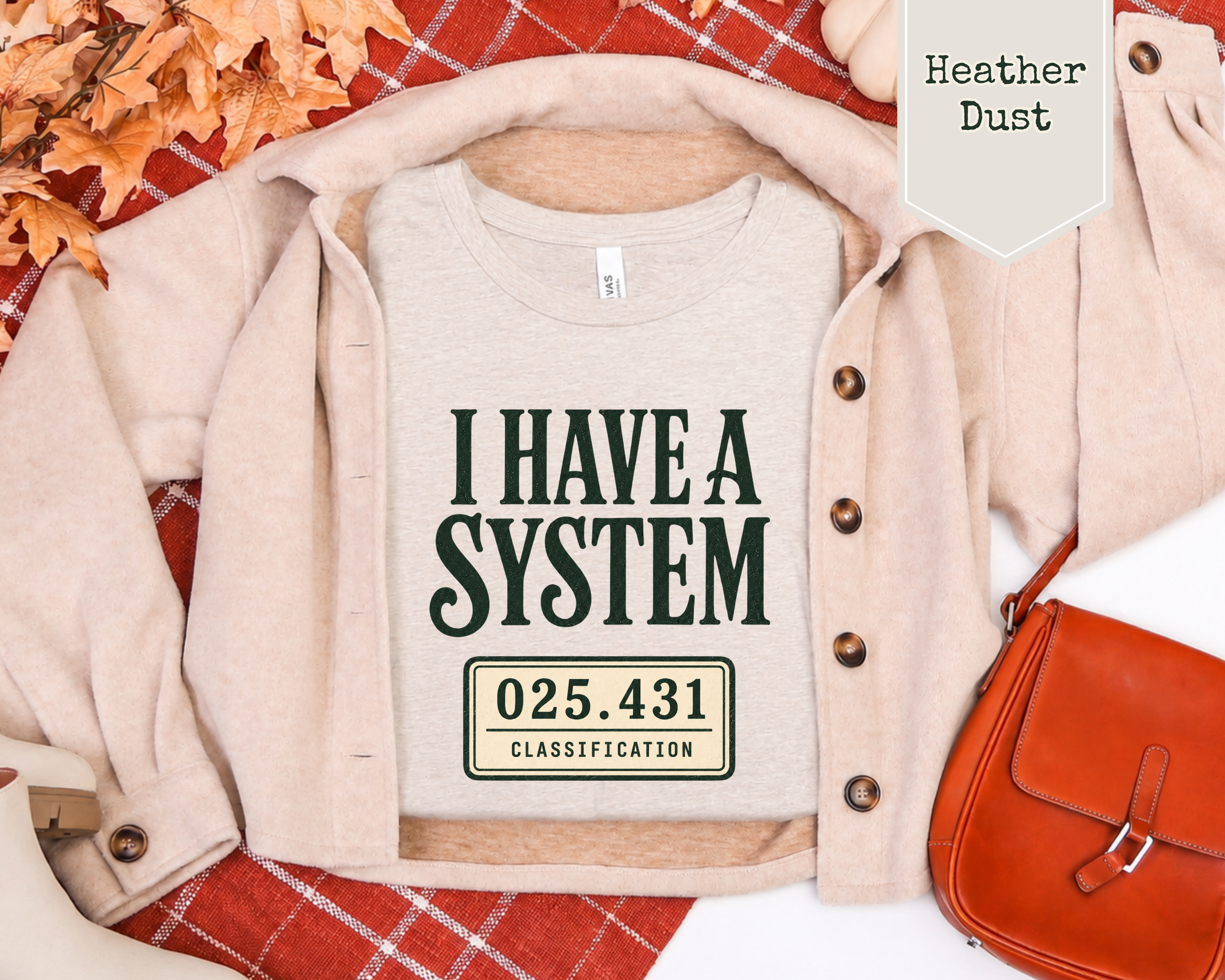 A flat-lay of a light heather gray t-shirt with a dark green graphic reading 'I HAVE A SYSTEM' and '025.431 CLASSIFICATION'.