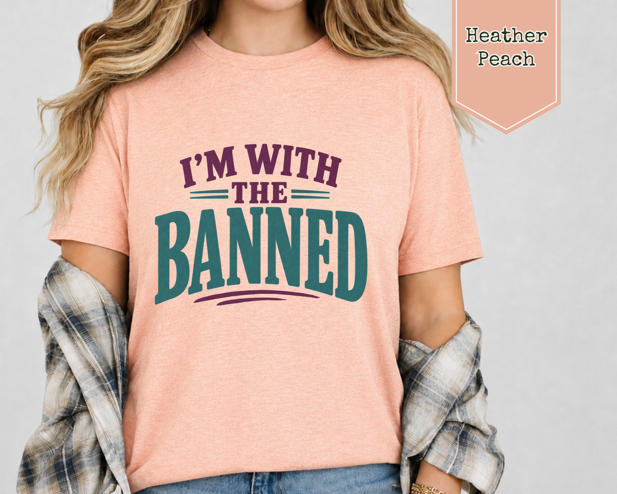 A woman wearing a heather peach t-shirt. The t-shirt with purple and green phrase of I'm With The Banned.