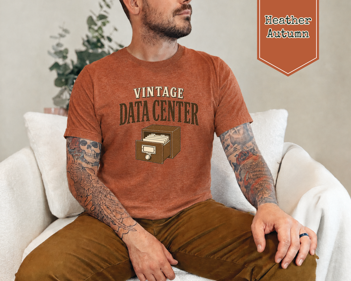 A man sitting on a chair wearing a heather autumn shirt. The tee shirt has a graphic on it that says Vintage Data Center with a vintage card catalog drawer.
