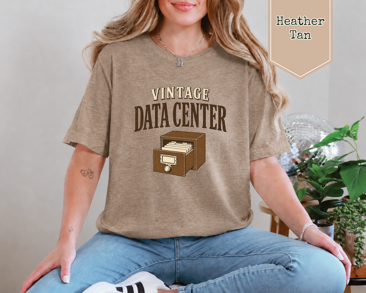 A woman sitting by a disco ball and some plants. The tee shirt has a graphic on it that says Vintage Data Center with a vintage card catalog drawer.