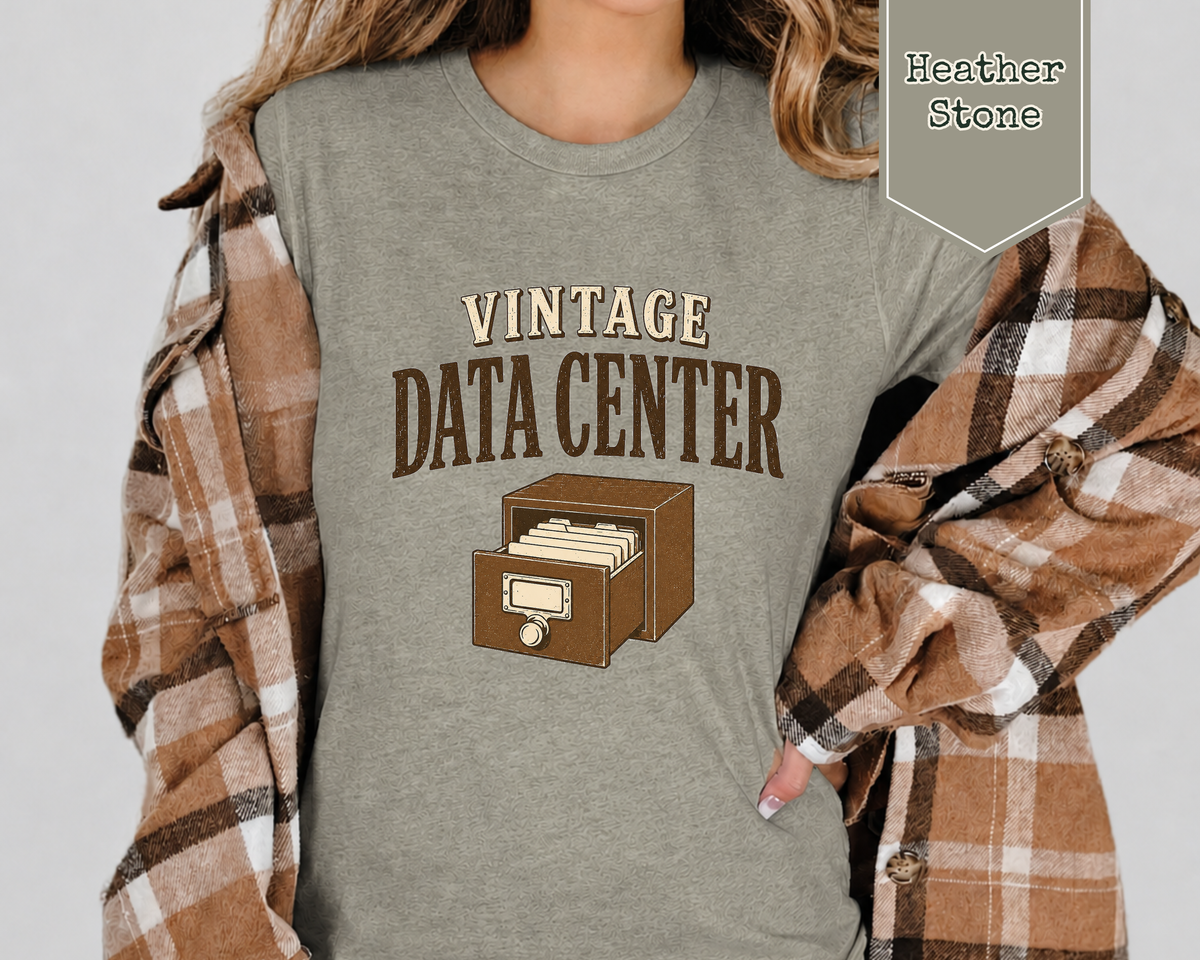 Woman wearing a heather stone tee shirt with a flannel top. The tee shirt has a graphic on it that says Vintage Data Center with a vintage card catalog  drawer.