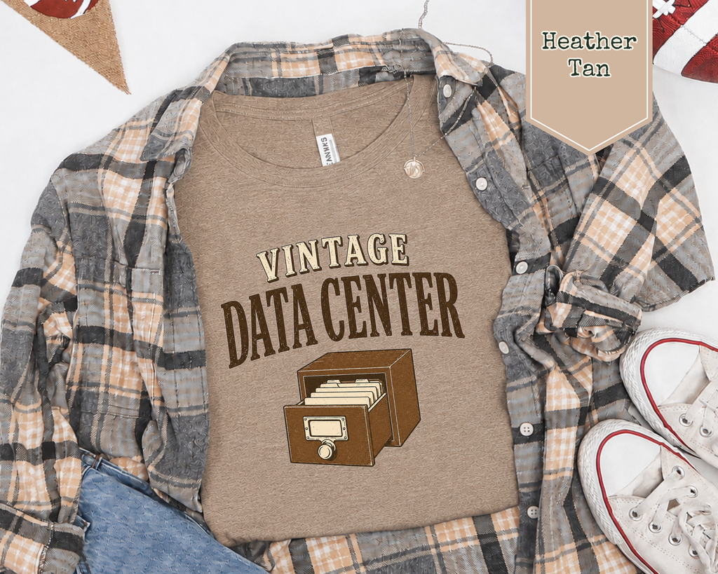 A heather tan flat lay t-shirt with a flannel, jeans, sneakers, and football decorations. The tee shirt has a graphic on it that says Vintage Data Center with a vintage card catalog drawer.