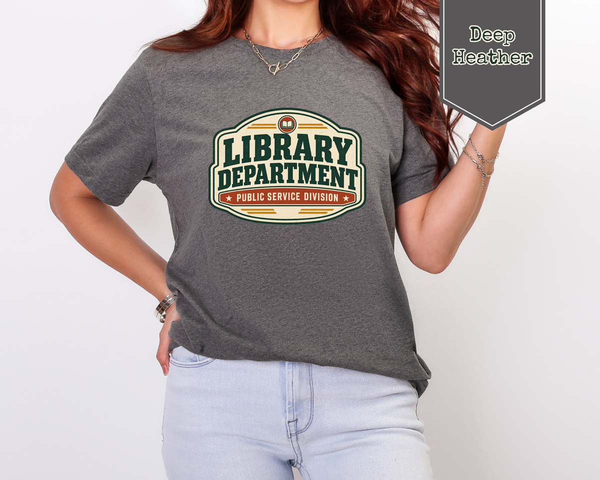 A woman wearing a dark heather gray t-shirt with a retro-style 'Library Department' graphic, paired with light blue jeans. A dark gray badge in the top right corner reads 'Deep Heather'.