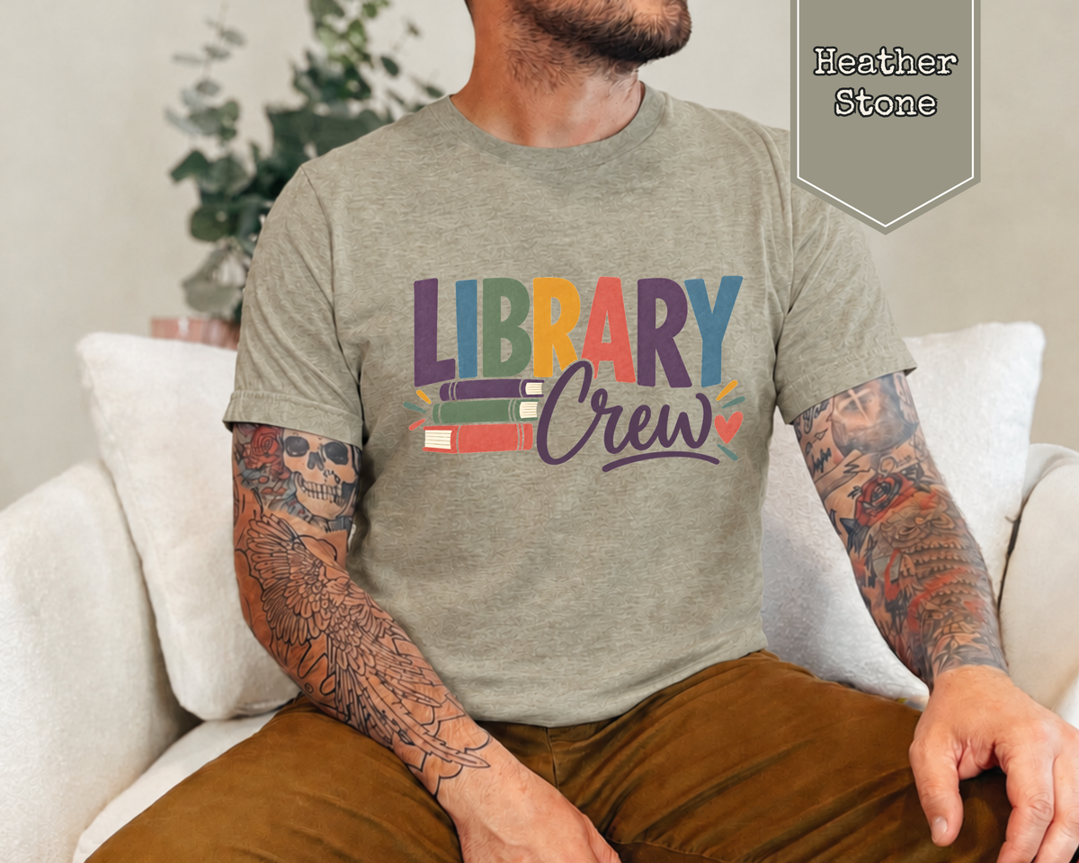 Man wearing a Heather Navy Library Crew t-shirt featuring colorful library book stack graphic.