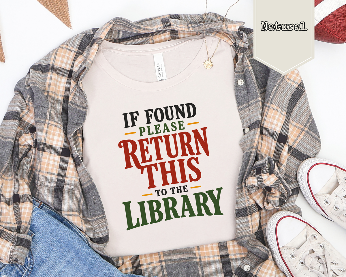 Flat lay of If Found Please Return to the Library shirt with paperback books and reading accessories.
