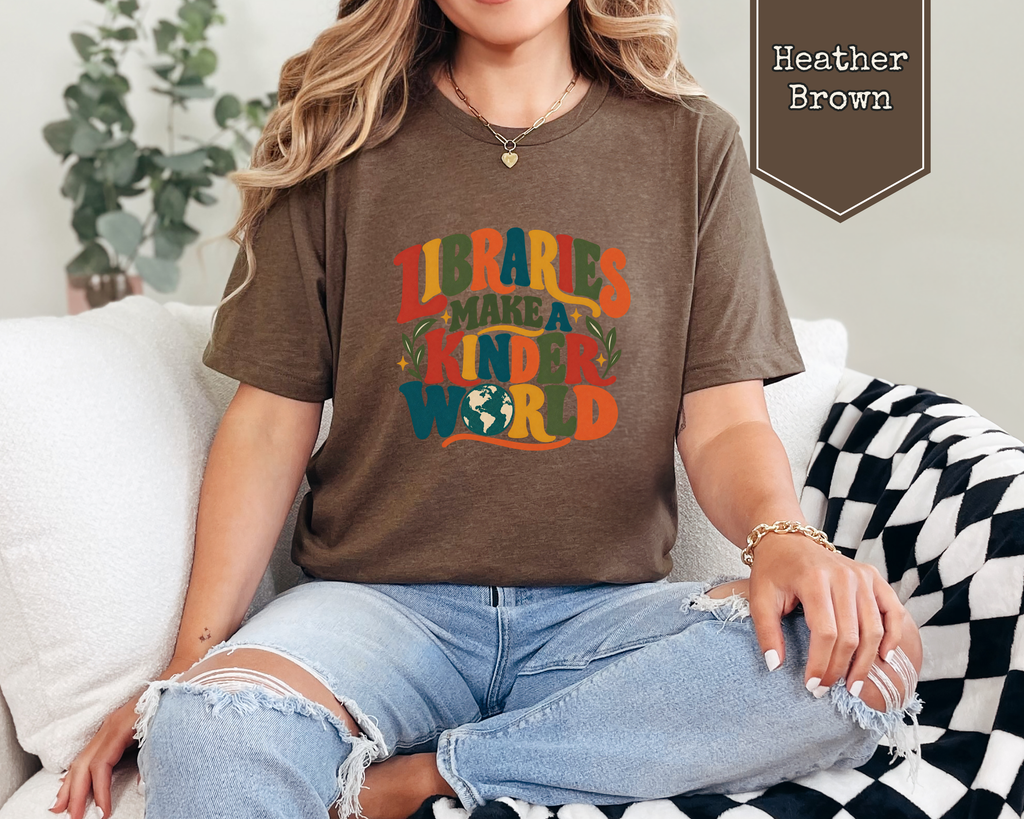 Woman wearing Steel Blue Libraries Make a Kinder World t-shirt in a cozy community library setting.