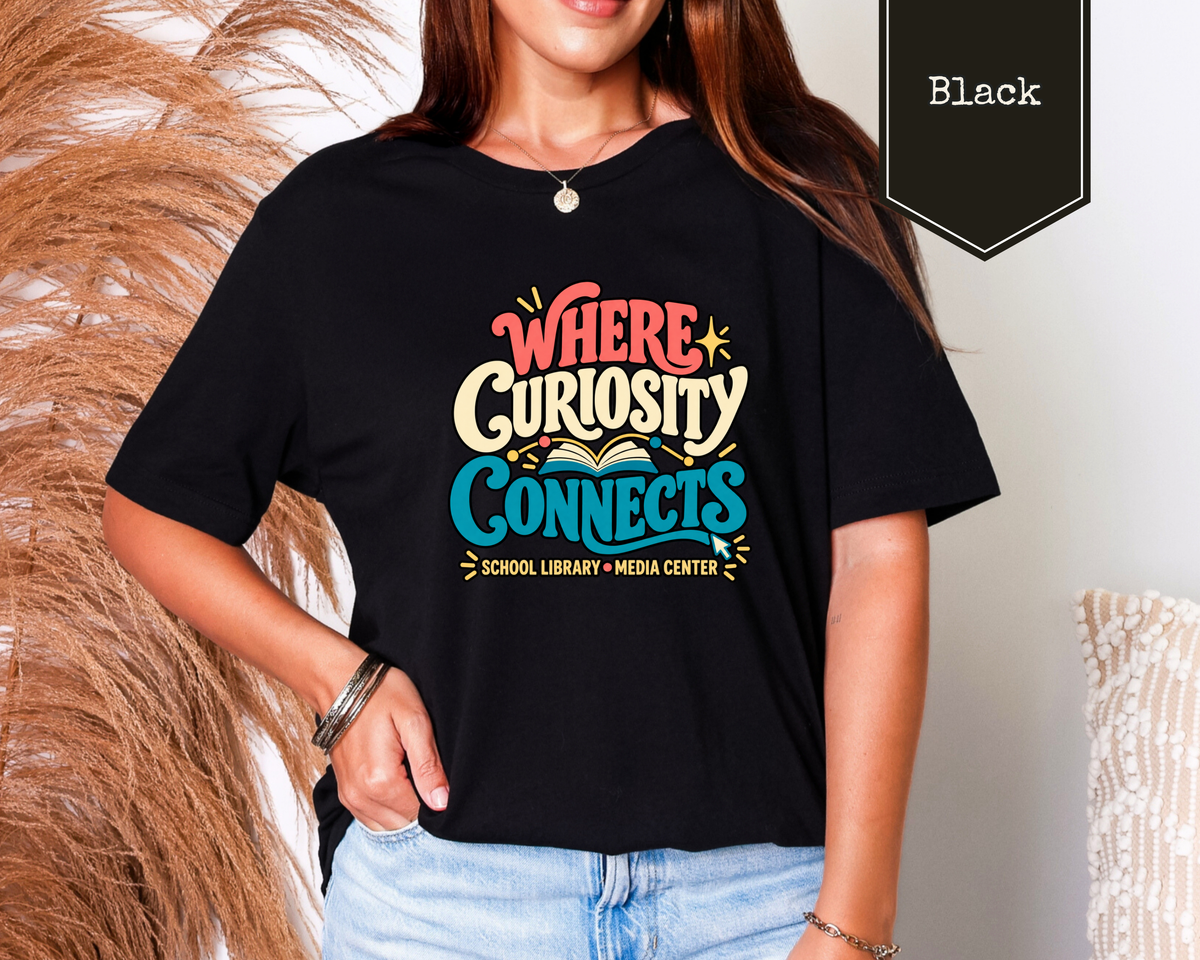 Woman wearing Heather Navy Where Curiosity Connects educator t-shirt in a modern library setting.