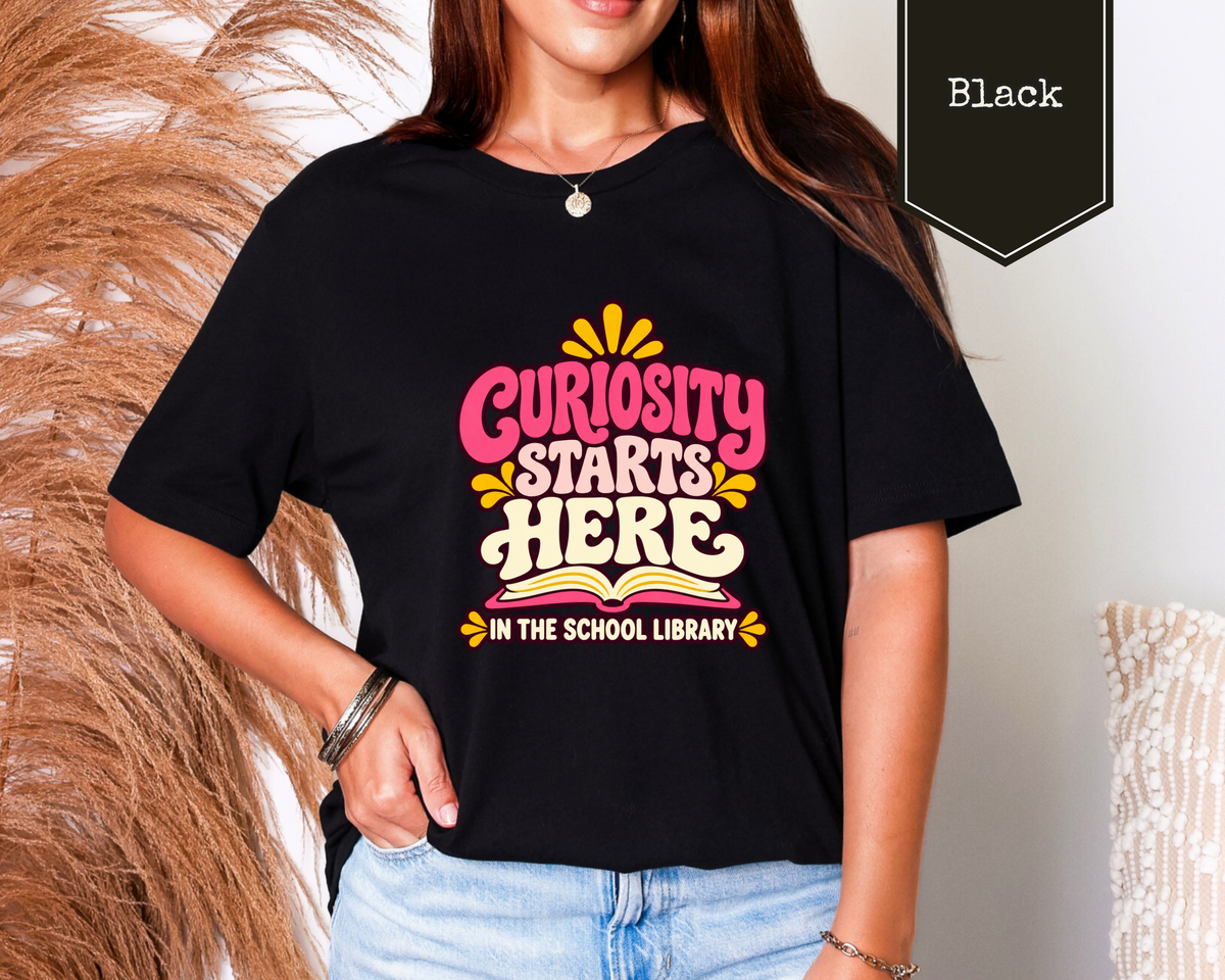 Man wearing Black Curiosity Starts Here school library graphic tee featuring retro typography.