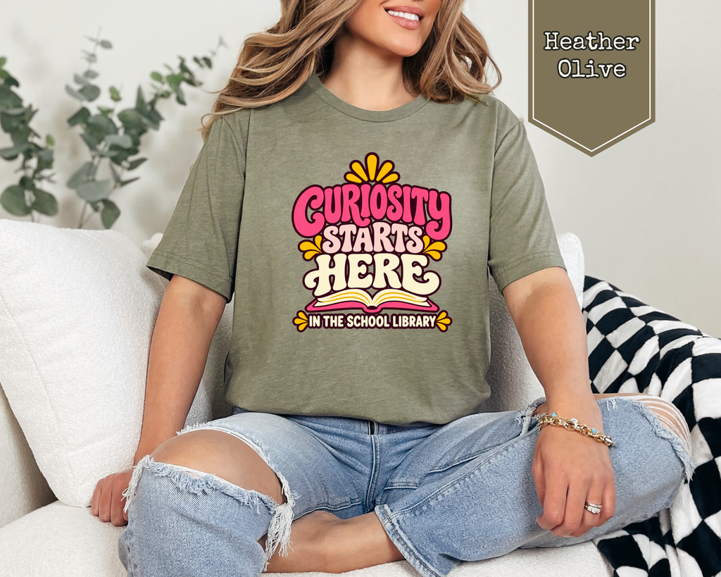 Person wearing Heather True Royal Curiosity Starts Here unisex graphic t-shirt.