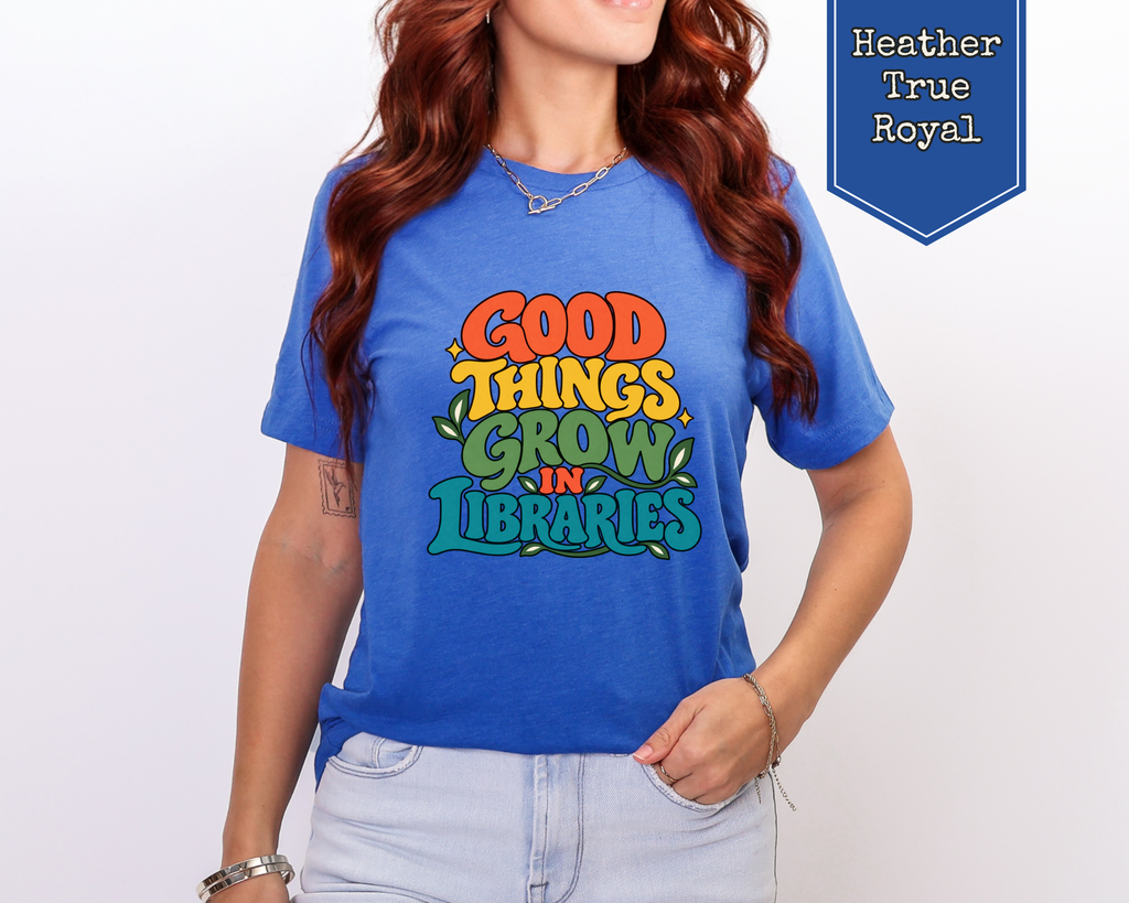 Woman wearing Heather Olive Good Things Grow in Libraries graphic tee in a sunlit reading room.
