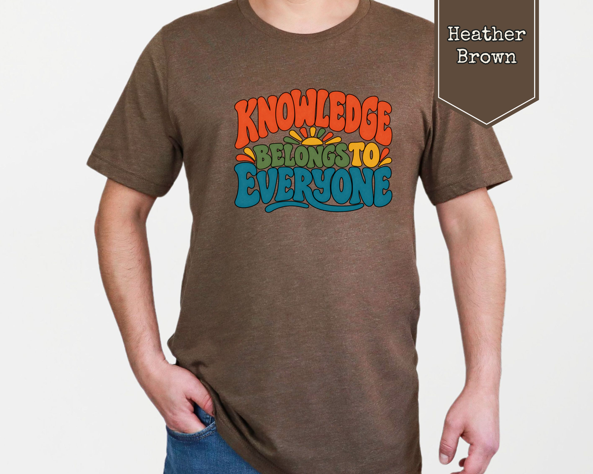 Person wearing Heather Prism Lilac Knowledge Belongs to Everyone unisex graphic t-shirt in a library setting.
