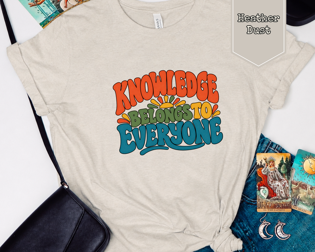 Folded Knowledge Belongs to Everyone graphic t-shirt styled in a flat lay with books, coffee mug, and reading accessories.