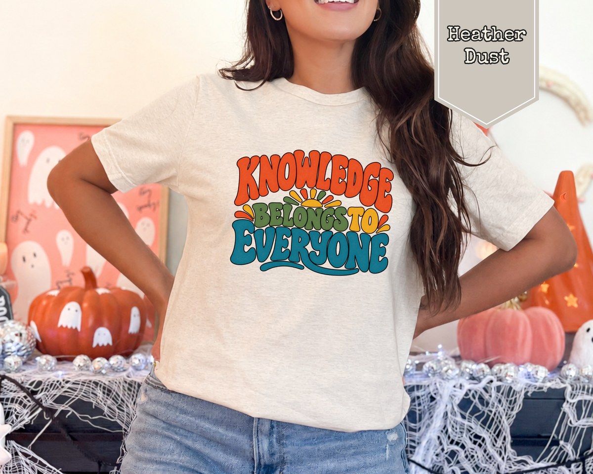 Woman wearing Heather Dust Knowledge Belongs to Everyone retro library advocacy graphic tee with colorful 1970s typography and sunrise illustration.