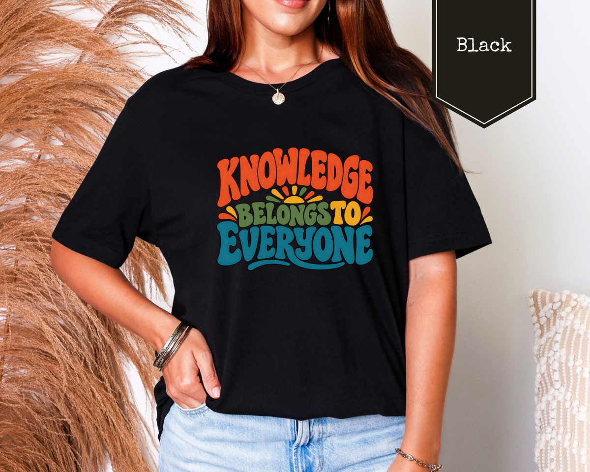 Man wearing Black Knowledge Belongs to Everyone graphic tee featuring colorful retro sunrise library artwork.